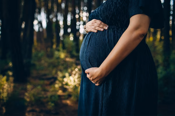 Pregnant woman holding belly while standing in forest